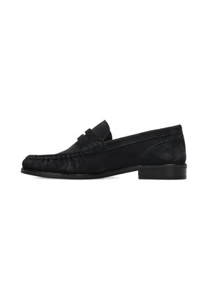 Mocassino in camoscio nero con tacco basso, punta arrotondata, cuciture visibili e dettaglio di fessura per penny sulla tomaia, mostrato di profilo su sfondo bianco.