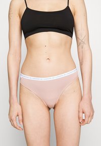 Rosa bomullsunderkläder i bikini stil med ett vitt elastiskt midjeband som har Lacoste-logotypen. Slät textur, låg midja design.