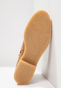 Scarpa in suede marrone con suola in gomma testurizzata, presenta una forma arrotondata e una soletta imbottita. La cucitura decorativa è visibile sulla parte superiore.
