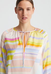 Mehrfarbige Bluse mit fließendem Design, leichtem Stoff, runder Ausschnitt mit Bindeband und horizontalen Streifen in Pastellfarben.