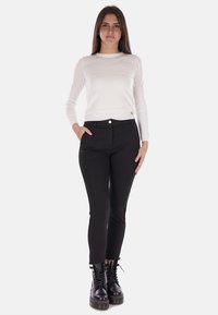 Pantaloni neri attillati con bottone frontale, abbinati a una camicia bianca a maniche lunghe. Modella che indossa stivali neri stringati con suola spessa.