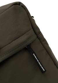 Sac à dos vert olive avec une texture lisse, présentant des coutures tonales et une étiquette en tissu noir intitulée "DOUBLE BY WOOD WOOD."