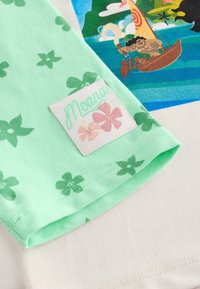 White fabric with a green floral-patterned sleeve features a Moana logo patch. The sleeve is cotton, soft, and lightweight.