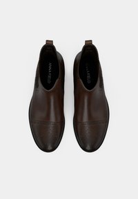 Cizme de gleznă din piele maro, cu o suprafață netedă, detalii brogue, panouri elastice pe laterale și tab. pentru tras. Vârf rotund și accente contrastante.