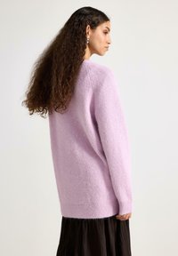 Lyse lilla, blød sweater med en afslappet pasform og ribbede manchetter, kombineret med et plisseret sort skørt. Tekstureret overflade synlig.