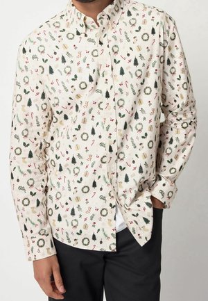 Chemise à col boutonné en tissu léger, fond crème avec des motifs de fête rouges et verts comprenant des couronnes, des sapins et des cannes en sucre.