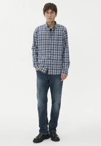 Mėlynas ir baltas languotas marškinėlių mygtukas ir tamsūs džinsai. Marškiniai turi apykaklę ir ilgomis rankovėmis, yra laisvo kirpimo su subtilia tekstūra.