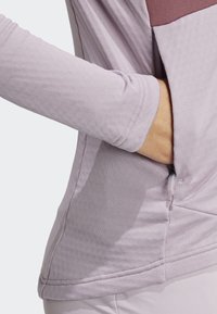 Svijetlopurple dugi rukav majica s teksturiranim materijalom, bočnim džepom sa zipom i kontrastnom bordo pločom preko grudi, s urednim šavovima.