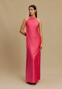 Hosszú rózsaszín szaténruha, horgotípusú nyakkivágással, sima textúrával, testhezálló sziluettel és finom fényű felülettel, fülbevalóval viselve.