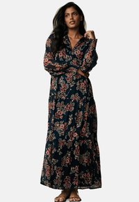 Maxi dress with a navy background, featuring floral patterns in shades of pink and green, long sleeves, and a tiered hem design.