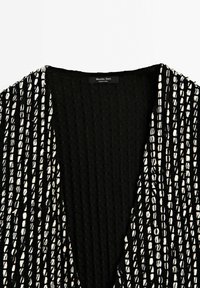 Czarna i biała sweterkowa odzież o teksturowanej powierzchni, z pionowymi paskami i głębokim kołnierzem w kształcie litery V, oznaczona marką Massimo Dutti, wyprodukowana w Indiach.