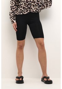 Czarne szorty rowerowe o gładkiej fakturze, wysokim stanie i dopasowanym kroju. Połączone z bluzką w panterkę i masywnymi czarnymi sandałami.