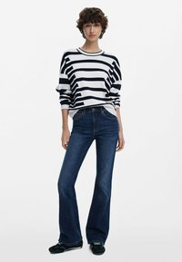Blauwe flare jeans gecombineerd met een wit en marineblauw gestreept sweatshirt. De stof lijkt zacht, met een relaxte pasvorm en een ronde hals.