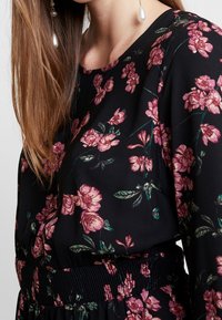 Black dress with pink floral pattern, featuring a rounded neckline and elastic waistband. Smooth fabric with a relaxed fit, accented by leaves.