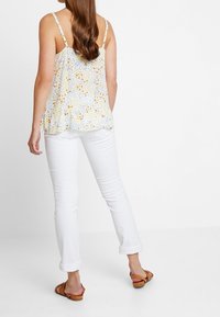 Top senza maniche con stampa floreale in un tessuto leggero e testurizzato; jeans bianchi in denim; sandali piatti marroni. Design della schiena in stile barca.