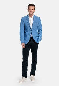  Lichtblauwe blazer met notched lapels, enkel knoopsluiting en pochet, gecombineerd met een witte shirt, zwarte broek en lichte sneakers.