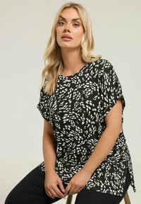 Czarny i biały, krótki top z wzorem nieregularnych plam, okrągły dekolt i boczne rozcięcia, w zestawie z czarnymi spodniami.