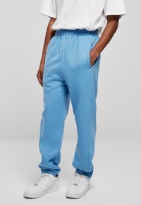 Lichtblauwe sweatpants met een elastische tailleband en boorden, voorzien van zijzakken en een gladde textuur. Gecombineerd met witte sneakers.