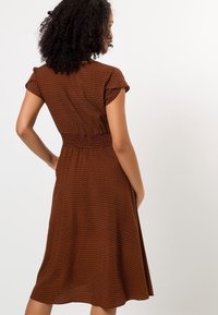 Brązowa sukienka w wzory z zygzakowym wzorem, krótkie rękawy, dopasowana talia i rozkloszowany dół. Gładka faktura materiału z luźnym krojem.