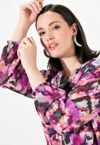 Blusa setosa e decorata con un design multicolore in varie sfumature di viola, rosa e nero. Maniche arricciate e morbido al tatto.