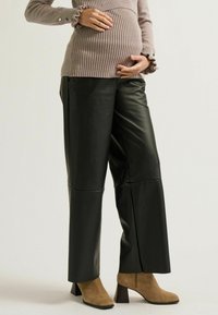 Schwarze, faux-lederne Weitbein-Hosen mit glatter Textur und klaren Linien, kombiniert mit einem Strickoberteil und taupefarbenen, geschlossenen Ankle-Boots.