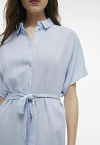 Abito camicia blu chiaro realizzato in un tessuto morbido, con chiusura a bottoni sul davanti, maniche corte e una cintura da annodare in vita.