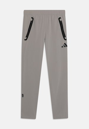Pantalons de sport grisés en tissu léger, dotés de poches zippées noires et d'un logo Adidas sur la cuisse supérieure gauche.