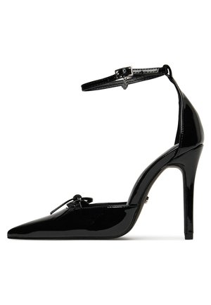 Zapato de tacón alto de charol negro con punta puntiaguda, correa en el tobillo y detalle decorativo de lazo en la parte delantera. Diseño de tacón de aguja.