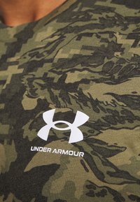 Grön kamouflage kortärmad t-shirt i bomull, med en vit Under Armour-logotyp på bröstet och ett strukturerat ytmönster.