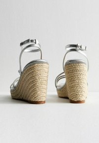 Silver metallic wedge sandals with braided jute heel, adjustable ankle strap, and textured detailing along the platform.