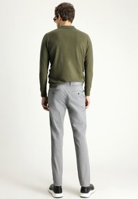 Camicia verde a maniche lunghe, pantaloni grigi e sneaker nere. I pantaloni presentano due tasche posteriori, una texture del tessuto liscia e una vestibilità su misura.
