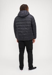 Black puffer jacket with a hood, featuring horizontal quilted sections. Worn over black pants and black sneakers with white soles.
