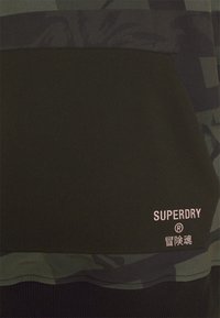 Dunkelgrüner Sweatshirt mit einem kontrastierenden gemusterten Oberpanel. Enthält eine Kängurutasche und ein gesticktes "SUPERDRY"-Logo in Hellrosa.