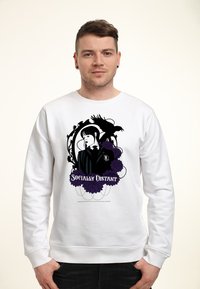 Uomo che indossa un felpa bianca con una grafica nera e viola di una ragazza, un corvo, fiori e il testo "Socialmente Distant" sul davanti.