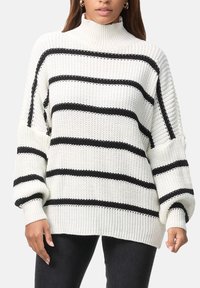 Pull blanc en maille avec des rayures horizontales noires, doté d'un col montant, de manches larges et d'une finition texturée côtelée.