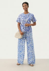 Ensemble en coton composé de deux pièces avec un motif abstrait bleu et blanc. Haut ample et pantalon large, complété par un sac en feutre.