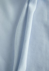 Tessuto azzurro chiaro che mostra intrecci lisci e testurizzati, con una cucitura visibile e modelli variabili di maglia e tessitura per un contrasto tattile.