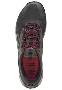 Cipele za trail trčanje u tamno sivoj i maslinastoj zelenoj boji, sa crvenim vezicama, teksturiranom površinom i gumenom potplatom s višesmjernim gaznim slojem.