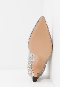 Pointed-toe high heel shoe in textured snakeskin pattern, beige with a light sheen, featuring a leather sole and small black heel.