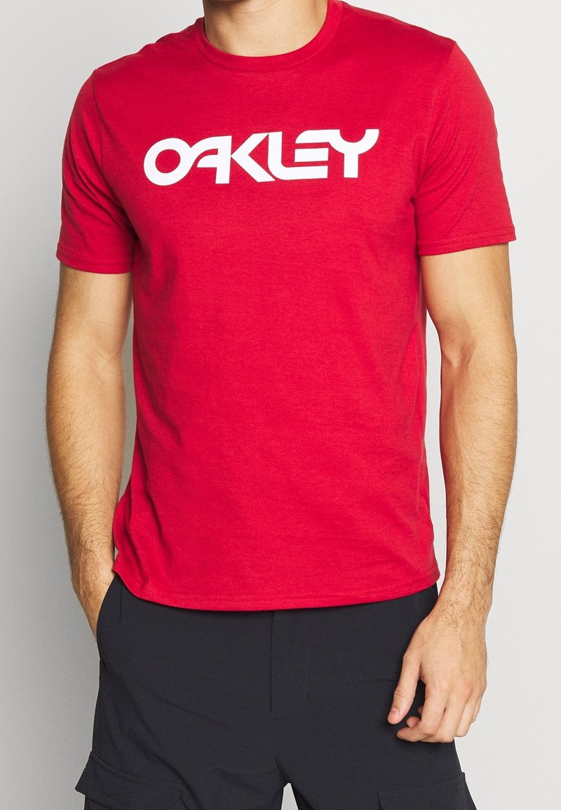 Czerwona bawełniana koszulka z krótkimi rękawami, z dużym białym logo "OAKLEY" na klatce piersiowej. Prosty, okrągły dekolt.
