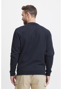 Sweatshirt blu navy in tessuto morbido, con scollatura a girocollo e maniche lunghe. La vista dal retro mostra una texture liscia senza pattern.