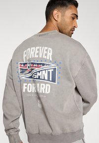 Γκρι φούτερ με μακριά μανίκια, με γραφικό με εφέ φθοράς στην πλάτη που γράφει «FOREVER FORWARD» και μπλε λεπτομέρειες με σχέδιο ποδοσφαιρικής μπάλας.