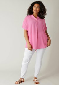 Camicetta rosa a maniche corte con un motivo a griglia testurizzata, caratterizzata da un colletto a V e tre bottoni, abbinata a pantaloni bianchi slim-fit e sandali.