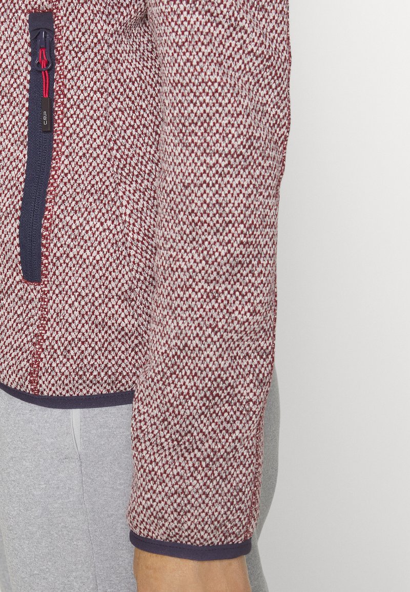 Giacca in pile a scacchi rossi e bianchi con accenti blu navy, dotata di zip frontale e polsini elasticizzati, che mette in risalto texture e dettagli di design.