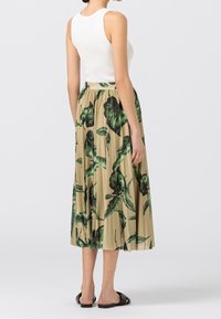 Vit ribbad linne i kombination med en lång beige kjol med gröna lövmönster och plisserad design, kompletterad med svarta sandaler.