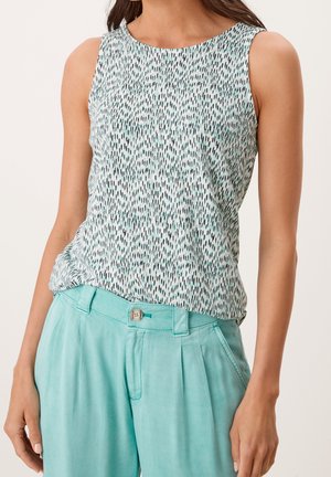 Bezrekawka biała bluzka z czarno-zielonym wzorem zestawiona z wysokim stanem, jasnoturkusowymi spodniami z guzikami i plisami.