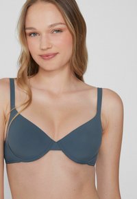 Modelowany szary biustonosz z gładkiego materiału, wsparciem w postaci fiszbin, regulowanymi ramiączkami oraz subtelnym dekoltem w kształcie litery V.