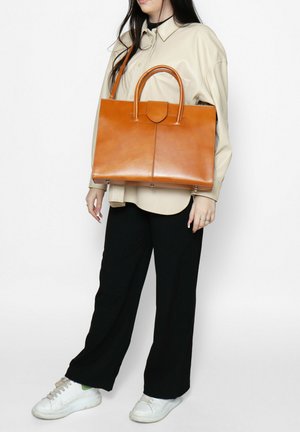 Oranje lederen schoudertas met twee bovenhandvatten, gestructureerde vorm, gladde textuur en zichtbare naaddetails. Draagt tegen een lichte achtergrond.