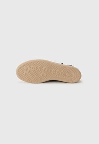Semelle d'une sneaker en caoutchouc, présentant un motif de grip texturé et un marquage. La couleur est beige avec une légère courbure pour le confort.