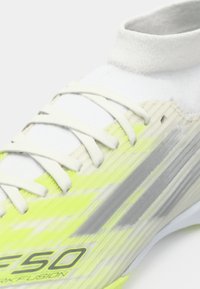 Λαμπερό κίτρινο και λευκό ποδοσφαιρικό παπούτσι με υφασμάτινη επάνω επιφάνεια, φέρει κορδόνια, κολάρο σαν κάλτσα και χαμηλό προφίλ.